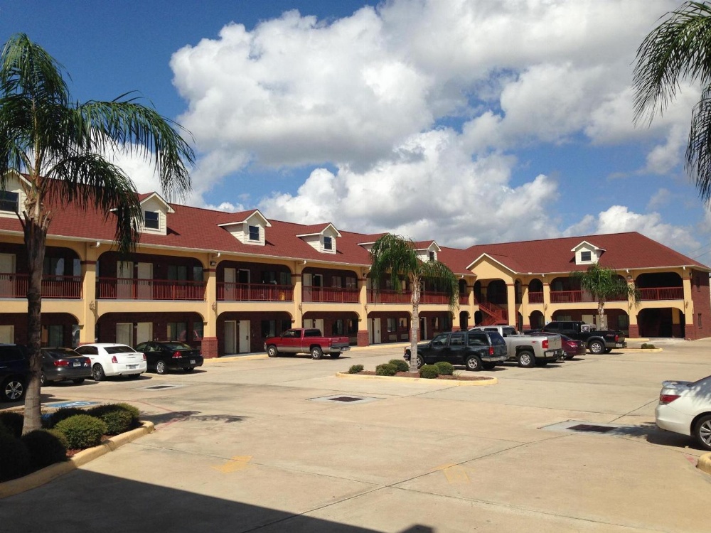 A two-story building with a red roof and yellow walls, surrounded by a parking lot and palm trees.