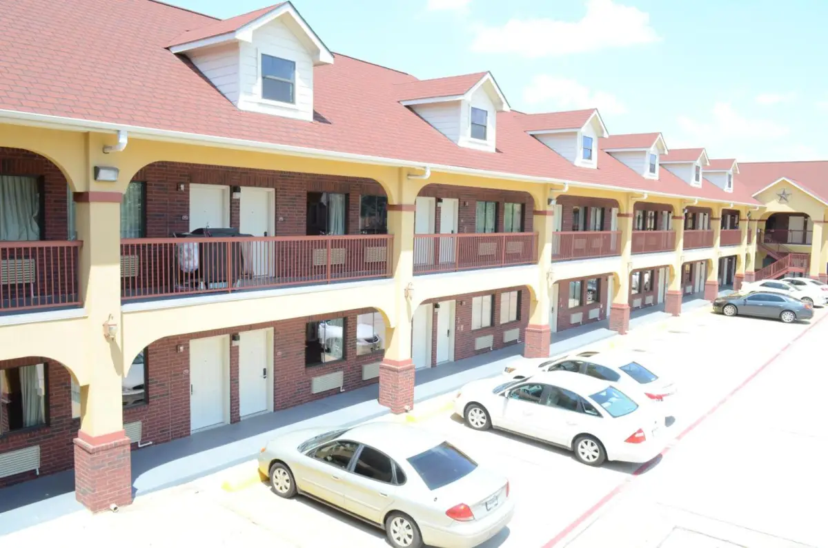 A two-story building with a red roof and yellow walls, featuring balconies and a parking lot.